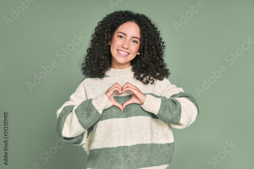 Young happy latin woman showing heart making shape with hands isolated on green background. Smiling female model expressing love and dating romance, warm affection, health care concept.