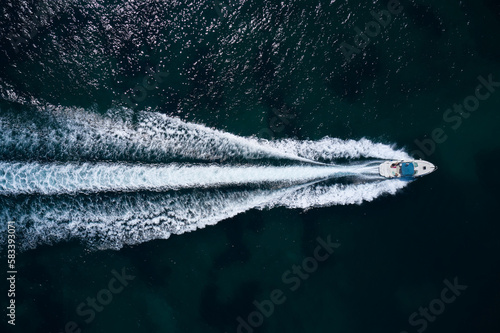 Big white boat with a blue awning fast movement on dark water top view.