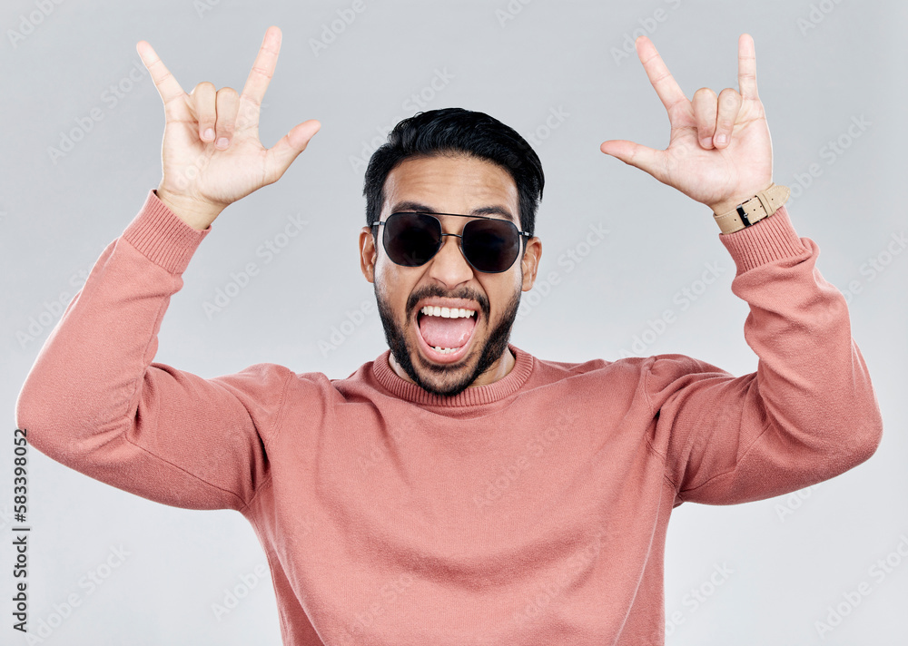 Naklejka premium Portrait, rocker and hand gesture with a man in studio on a gray background feeling crazy or energetic. Face, rock on or hardcore and a male posing with a devil horns sign or symbol at a concert