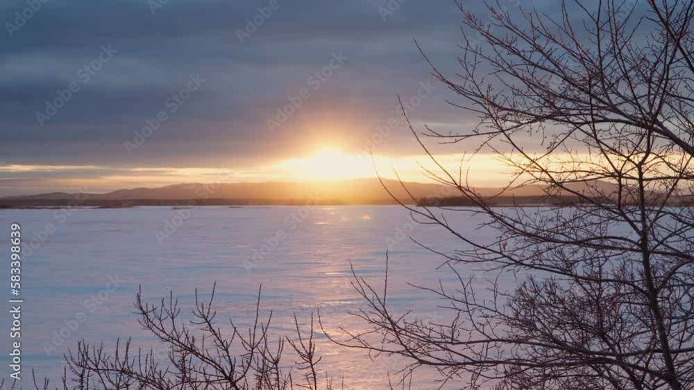 A beautiful sunset on a frozen lake with a mountain range and a forest in the background. A beautiful sunset on a frozen lake with a mountain range and a forest in the background.