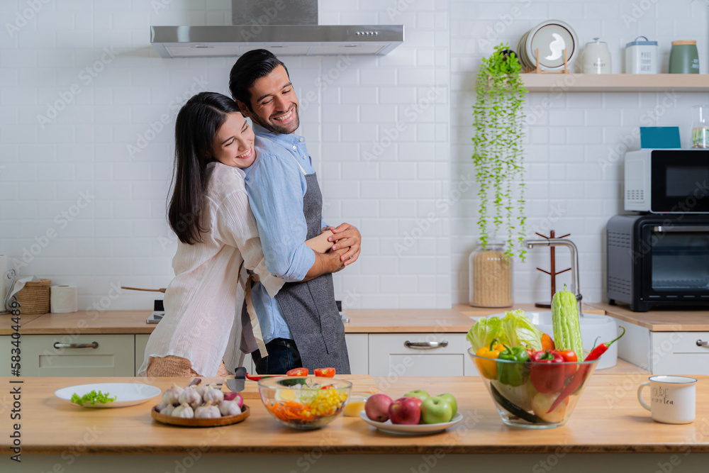 A woman happily hugs a man, a happy couple. Young couple in love having fun while preparing a breakfast together on a beautiful morning. Cooking, together