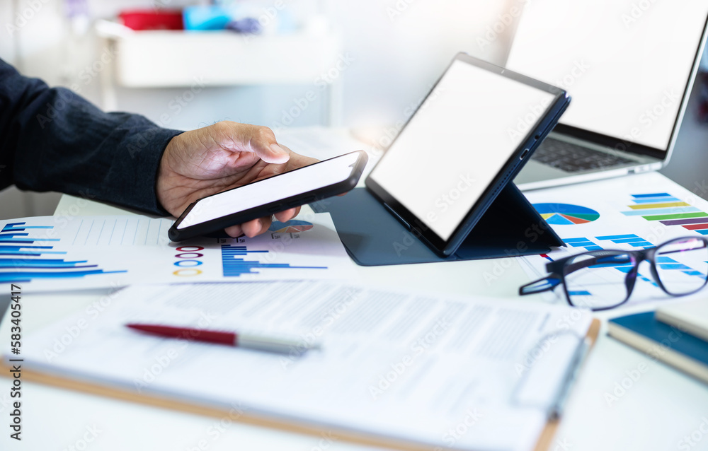 Asian businessman using smart phone to searching stock market data, Successful business people using laptop and tablet computer to analysis investment plan with chart on paperwork, Close-up view Asian businessman using smart phone to searching stock market data, Successful business people using laptop and tablet computer to analysis investment plan with chart on paperwork, Close-up view