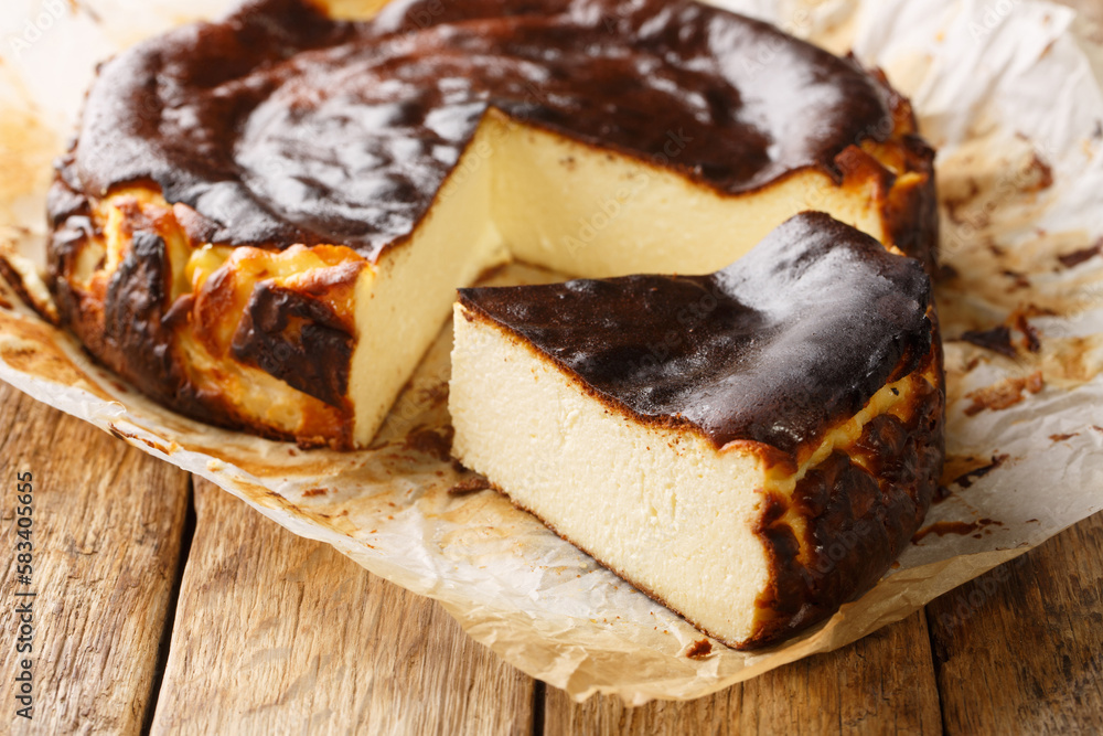 Fototapeta premium Rustic Fresh and delicious homemade Basque cheesecake closeup on the parchment paper on the wooden table. Horizontal