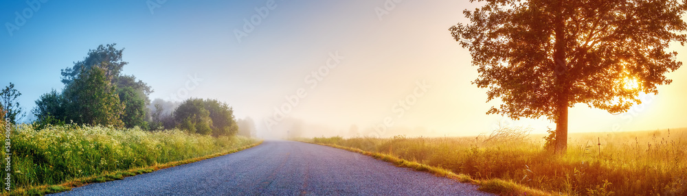 Obraz premium Sunrise in the foggy morning on the empty asphalt country road.