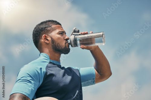 Drinking water, fitness and training with a sports man outdoor for a competitive game or event. Exercise, hydration and health with a male athlete taking a drink from a bottle during a break or rest