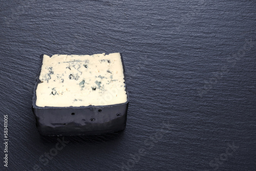 top view of tasty piece cheese with blue mold on black slate background, copy space