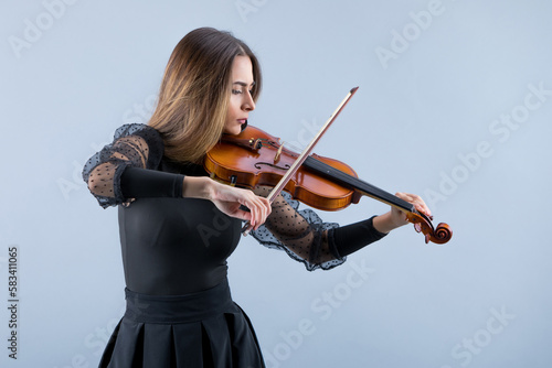 Violinist woman in the evening gown on the grey background.