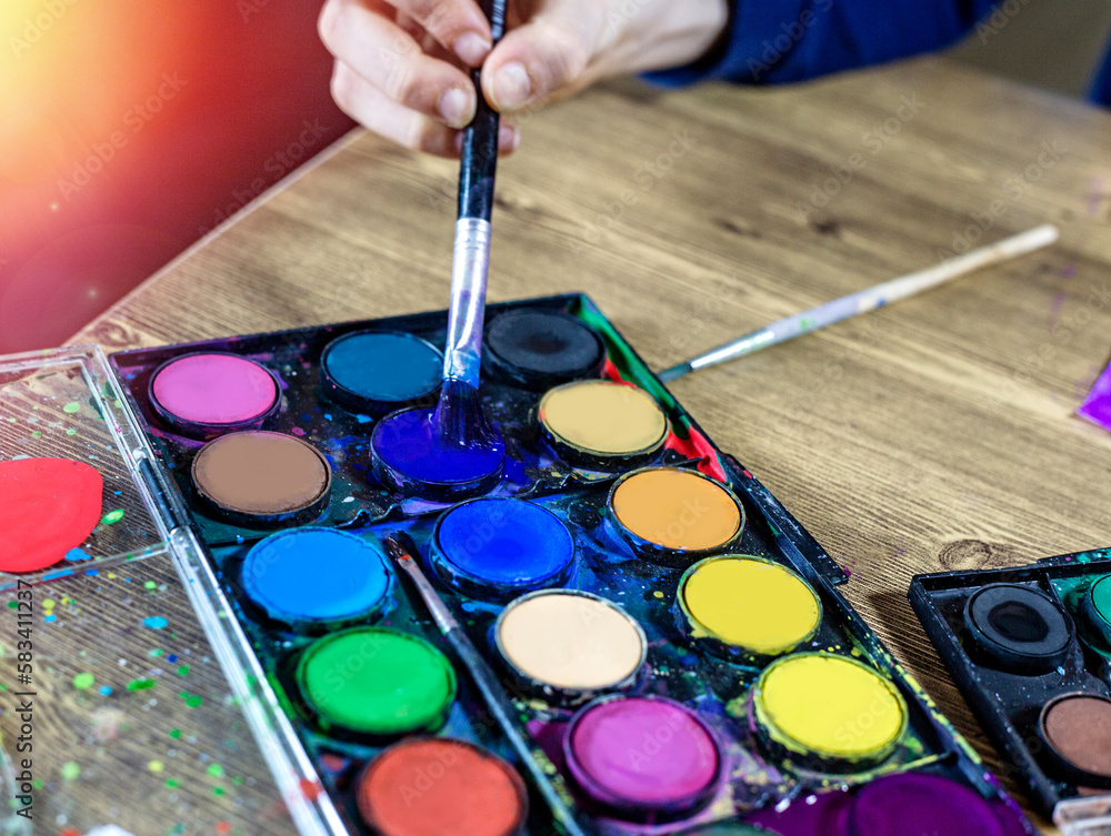 child creating drawing with multicolored paints and brush on wooden table close up child creating drawing with multicolored paints and brush on wooden table close up