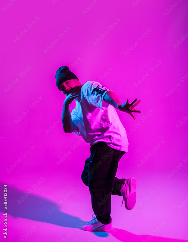 Handsome professional break dancer guy in trendy fashion clothes dancing in creative studio with pink and neon light