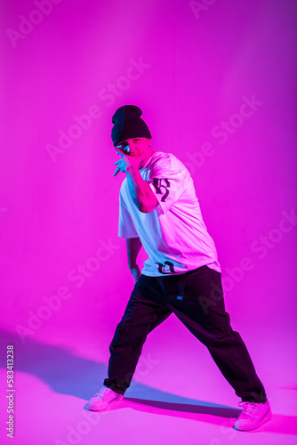 Handsome cool professional breakdancer guy in trendy clothes dancing in bright color studio with pink and neon lights