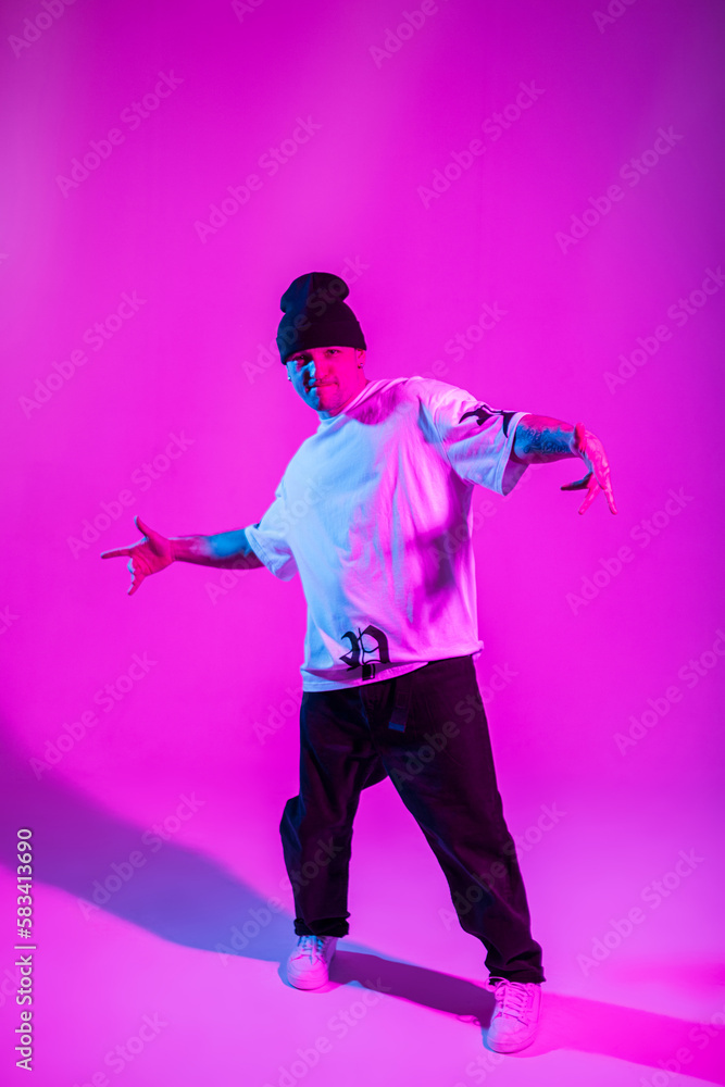 Professional b-boy dancer man in trendy fashion clothes with hat posing in creative studio with pink and neon light Professional b-boy dancer man in trendy fashion clothes with hat posing in creative studio with pink and neon light