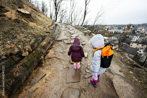 Two girls sisters walk up the wet path to an ancient fortress in rain. © AS Photo Family