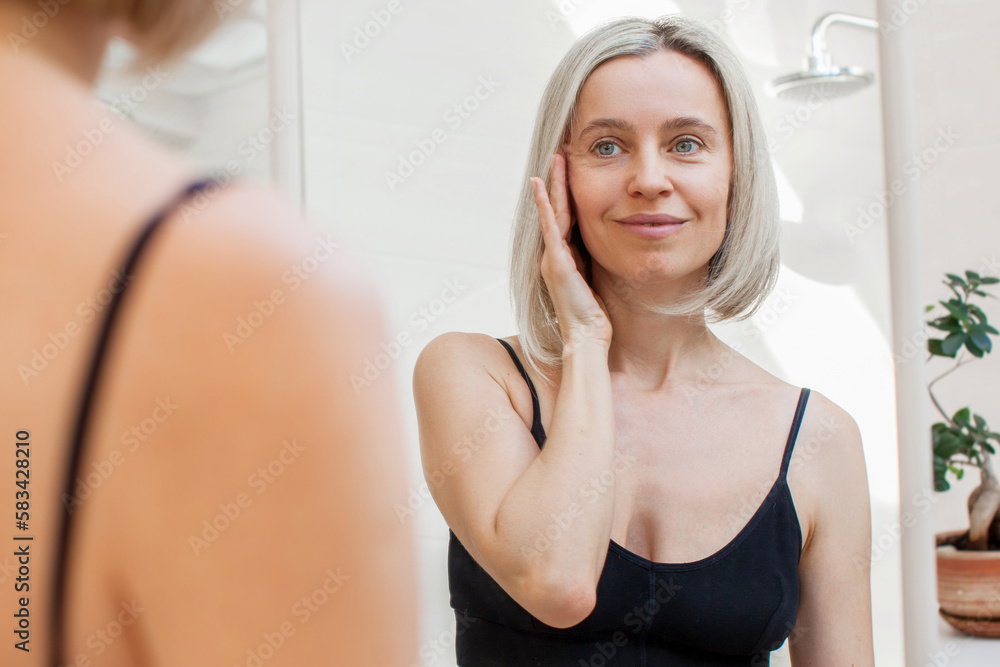 Middle aged Caucasian woman enjoys looking at her reflection in the mirror