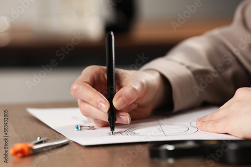 Jeweler drawing sketch of elegant ring on paper at wooden table indoors, closeup
