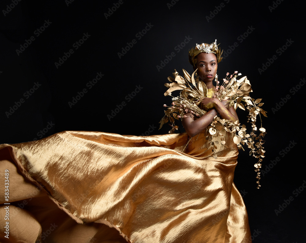fantasy portrait of beautiful african woman model with afro, goddess silk robes and ornate floral wreath crown. gestural Posing holding golden flowers. isolated on dark studio background fantasy portrait of beautiful african woman model with afro, goddess silk robes and ornate floral wreath crown. gestural Posing holding golden flowers. isolated on dark studio background