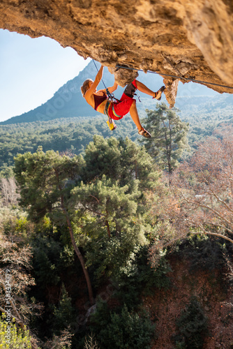 Girl climber on an overhanging rock. A sports woman climbs a rock against the backdrop of mountains. difficult movements in rock climbing.