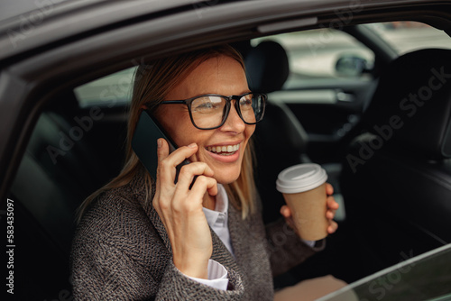 Woman with coffee talking phone and sitting on backseat of taxi and looking at window on way to work
