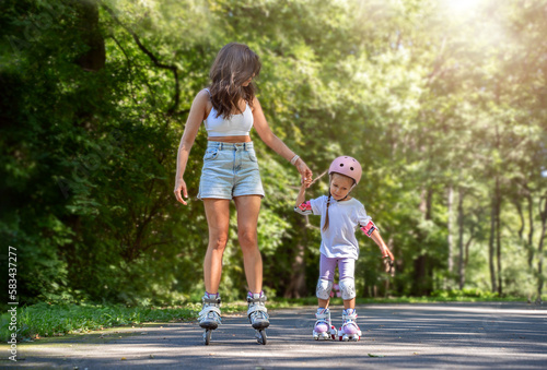 Mother teaching child daughter to skate on inline skates rollers in public park in summer. Family leisure outdoor sport activity game. Copy negative space
