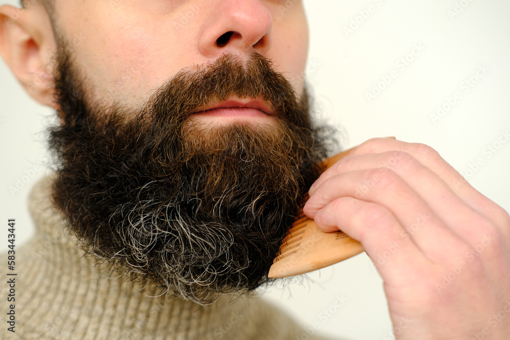 close-up of male face, young bearded and mustachioed man, guy with 25 - 30 years combs his thick beard, concept of mustache and beard stubble care products, hairline hygiene on lower part of face close-up of male face, young bearded and mustachioed man, guy with 25 - 30 years combs his thick beard, concept of mustache and beard stubble care products, hairline hygiene on lower part of face