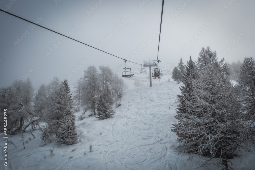 Ski lift transports skiers and snowboarders in foggy day at snowy mountain. Frozen funicular. Pinzolo and Madonna di Campiglio ski resort. January 2023 Ski lift transports skiers and snowboarders in foggy day at snowy mountain. Frozen funicular. Pinzolo and Madonna di Campiglio ski resort. January 2023