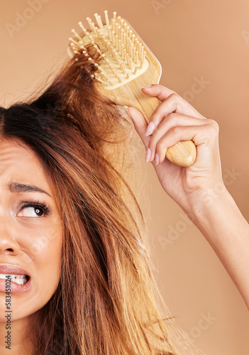 Sad woman, messy hair and brush for knots, tangle or haircare treatment against a studio background. Frustrated female brushing entangled hairdo, loss or curly frizz struggling to untie hairy knot photo