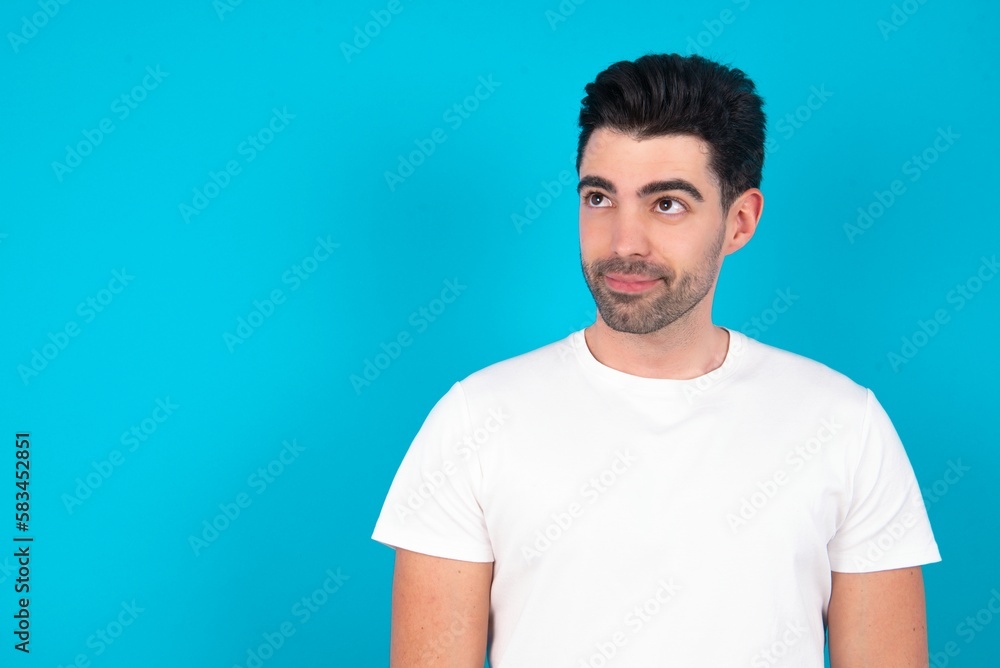 Obraz premium Young man wearing white T-shirt over blue studio background looking aside into empty space thoughtful