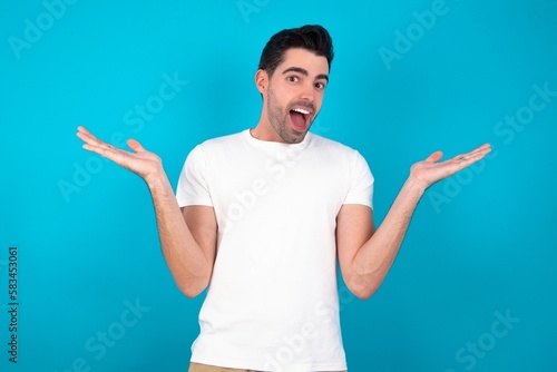 Young man wearing white T-shirt over blue studio background celebrating crazy and amazed for success with arms raised and open eyes screaming excited. Winner concept