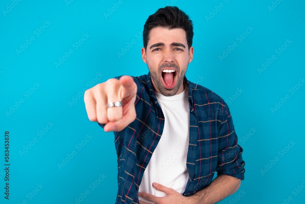 Young man standing over blue studio background pointing displeased and frustrated to the camera, angry and furious ready to fight with you. Young man standing over blue studio background pointing displeased and frustrated to the camera, angry and furious ready to fight with you.