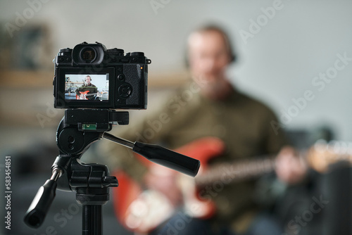 Close-up of professional camera standing on tripod with guitarist recording his performance on camera