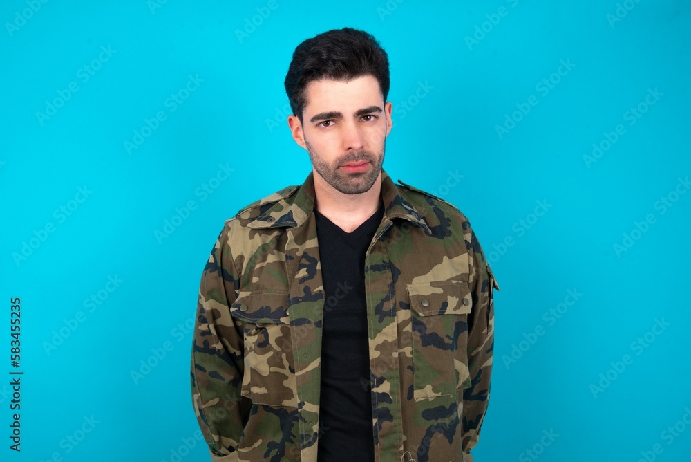Displeased Young man standing over blue studio background frowns face feels unhappy has some problems. Negative emotions and feelings concept