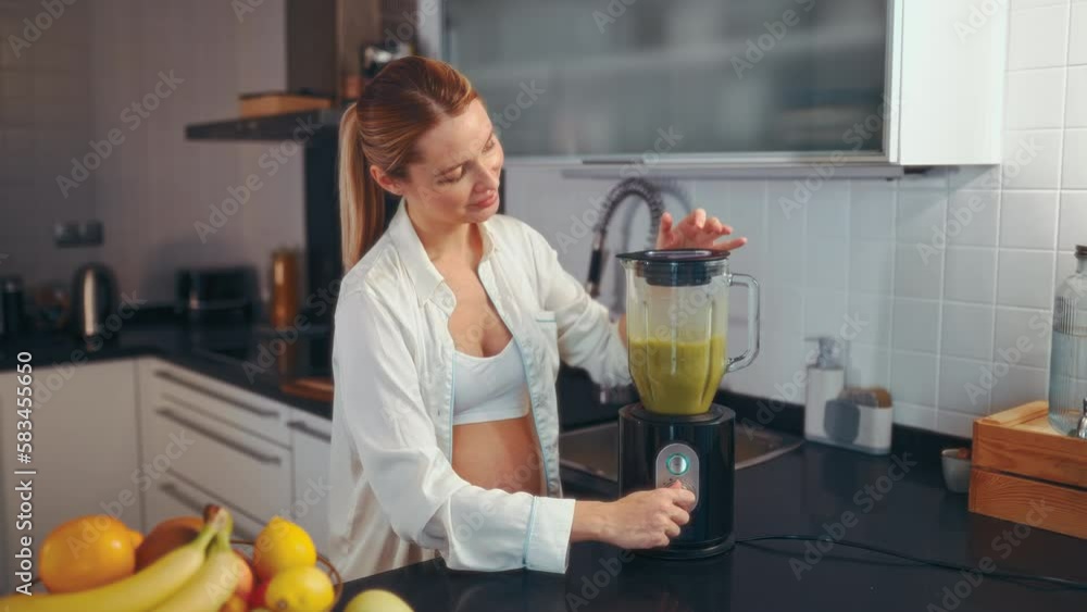 A young pregnant woman is preparing a smoothie with a blender in the kitchen. A pregnant woman drinks a vitamin smoothie. The concept of healthy eating during pregnancy. A young pregnant woman is preparing a smoothie with a blender in the kitchen. A pregnant woman drinks a vitamin smoothie. The concept of healthy eating during pregnancy.