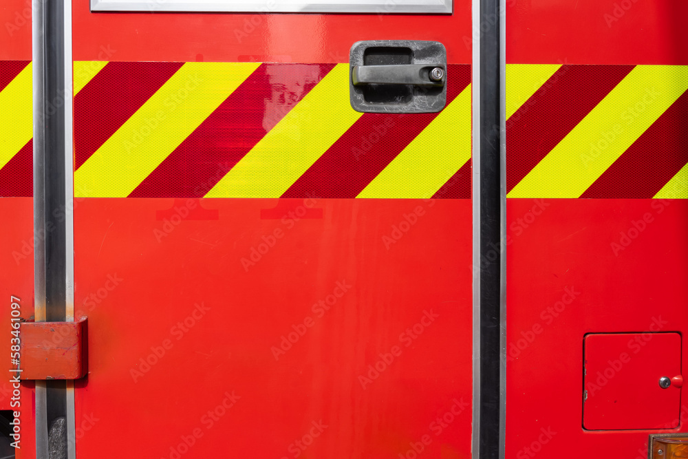 Door of a red fire truck with warning stripes and some red for copy