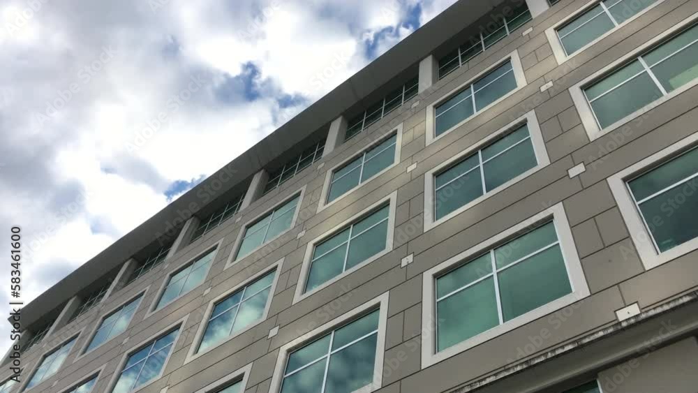 The motion of cloudy sky with illuminated reflected glass facade on modern office building The motion of cloudy sky with illuminated reflected glass facade on modern office building
