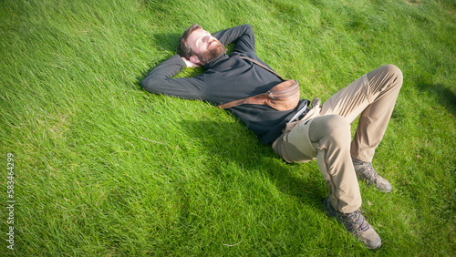 Hombre barbudo con riñornera de piel tumbado en pradera de hierba photo