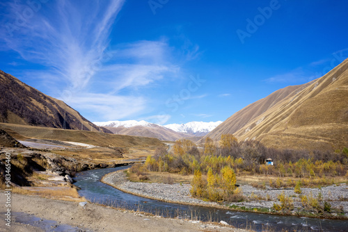 A river flows through the dry yellow Truso Valley near Stepantsminda in Georgia. Hills with dry grass and blue sky above. photo