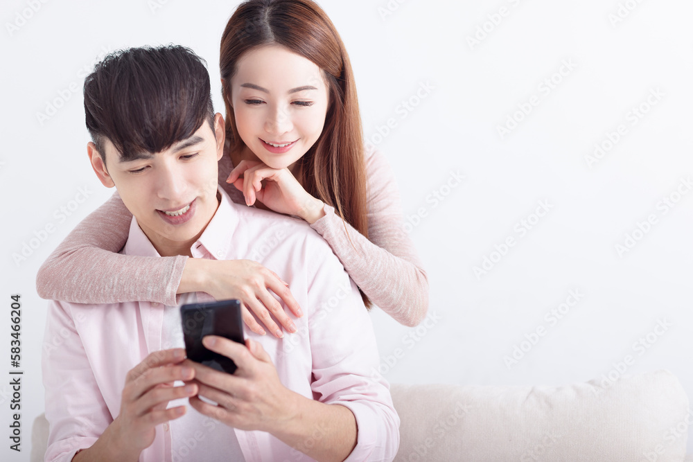Happy young Asian couple using mobile phone , browsing internet, chatting online, relaxing on sofa at home Happy young Asian couple using mobile phone , browsing internet, chatting online, relaxing on sofa at home