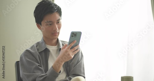 ソファに座ってスマートフォンを操作する若い男性