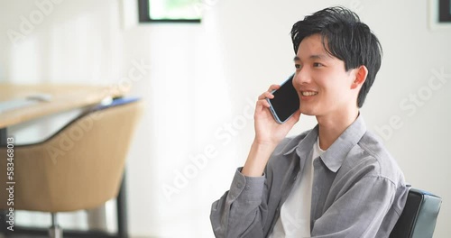 ソファに座ってスマートフォンで通話する若い男性