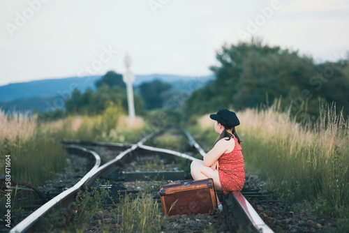 A little girl in a dress sits on an abandoned railroad tracks.