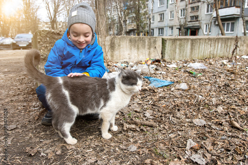 a little boy strokes a cat on the street. soft focus homeless animals photo