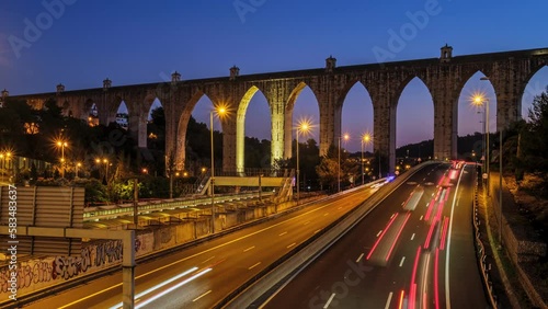 Time-lapse of highway traffic near Campolide station with Aguas Livres Aqueduct in background in the evening with car lights trails. Lisbon, Portugal. Zoom out effect photo