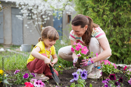 mother and child daughter plant flowers in the garden near the houme on spring day. Kid help mom work in the garden. slow life. enjoy the little things. 