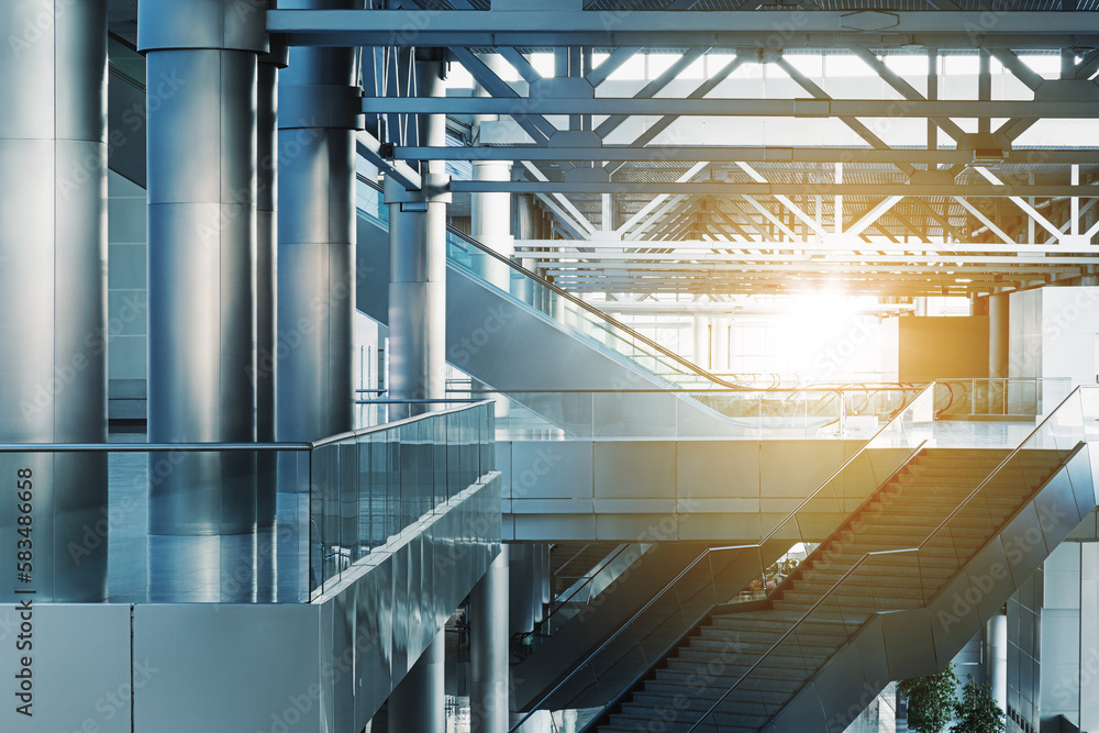 Escalators and stairs in modern office building, airport or transport terminal, glass walls and reflective floor; natural light and flare