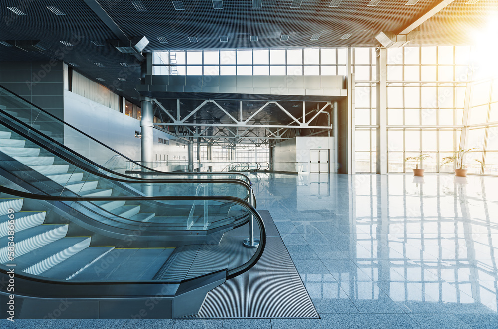 Escalators and stairs in lobby of modern office building, airport or shopping mall, glass walls and reflective floor, natural light and flare