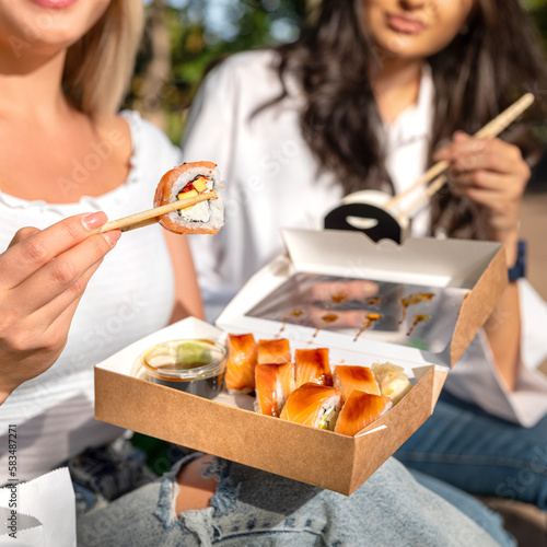 Friends young girls, girlfriends sit cute outdoors in nature, takeaway food, takeaway paper box close up.