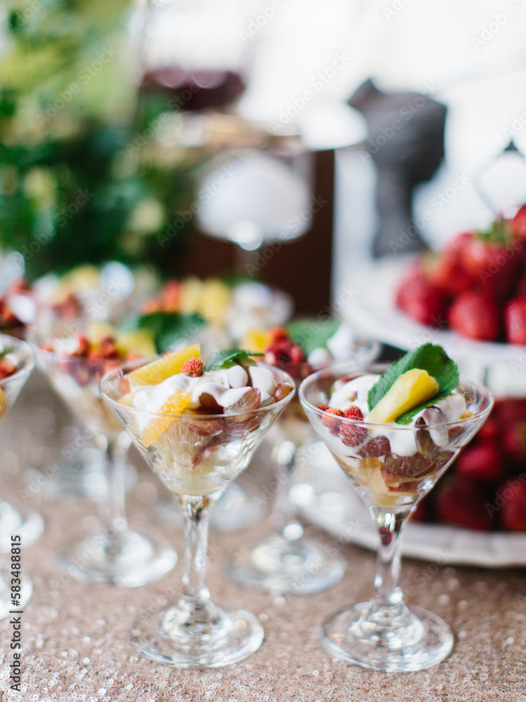 Naklejka premium Decorated outdoor buffet. Dessert of berries and croutons with whipped cream in glass bowls. In the background are fruits and greens.