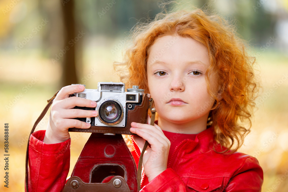 Little red-haired girl with a retro camera on an autumn background.Little red-haired girl with a retro camera on an autumn background.Close-up of the girl's face with a vintage camera.