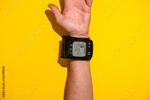 Blutdruckmessgerät am Handelenk eines Manns vor gelben Hintergrund, top view photo