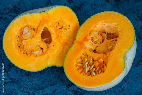 ripe orange pumpkin close-up cut into halves and seeds inside on a blue background, ripe healthy vitamin dietary vegetable,
