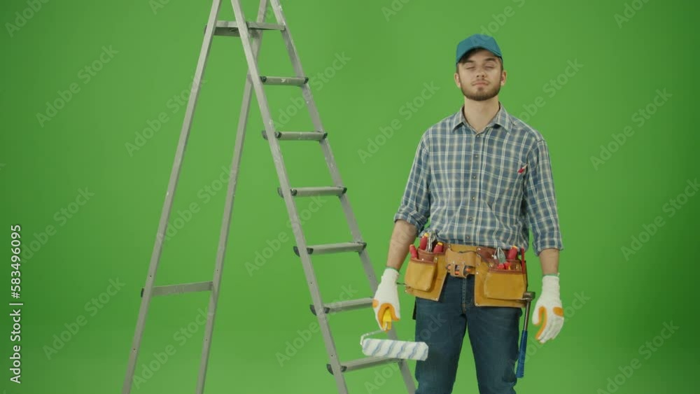 Green Screen.Young Bearded Confident Civil Engineer Wearing Checkered Shirt,Blue Cap and Leather Tool Belt,Lifting the Paint Roller Up,Making OK Gesture, Looking at Camera Smiling near the StepLadder Green Screen.Young Bearded Confident Civil Engineer Wearing Checkered Shirt,Blue Cap and Leather Tool Belt,Lifting the Paint Roller Up,Making OK Gesture, Looking at Camera Smiling near the StepLadder